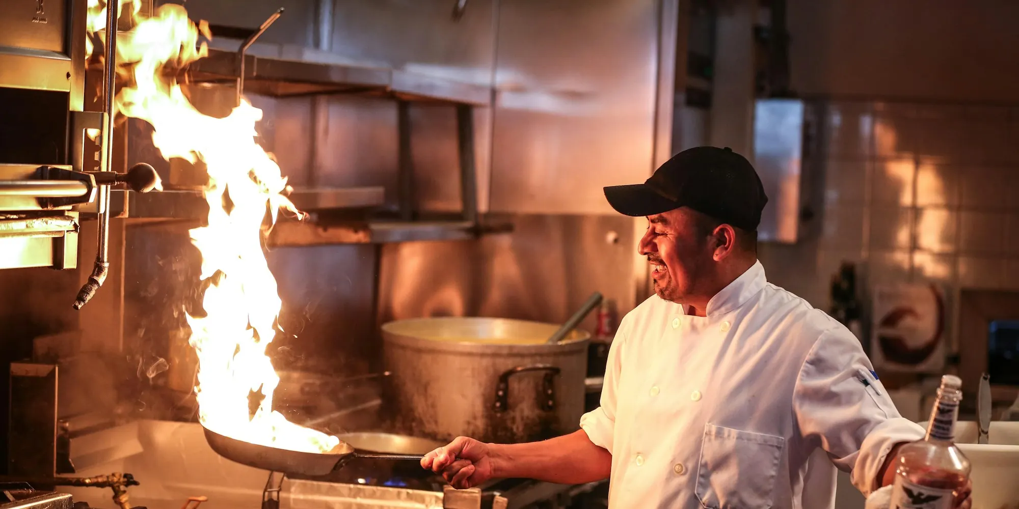 Chef in a white uniform cooking over a flaming pan in a restaurant kitchen
