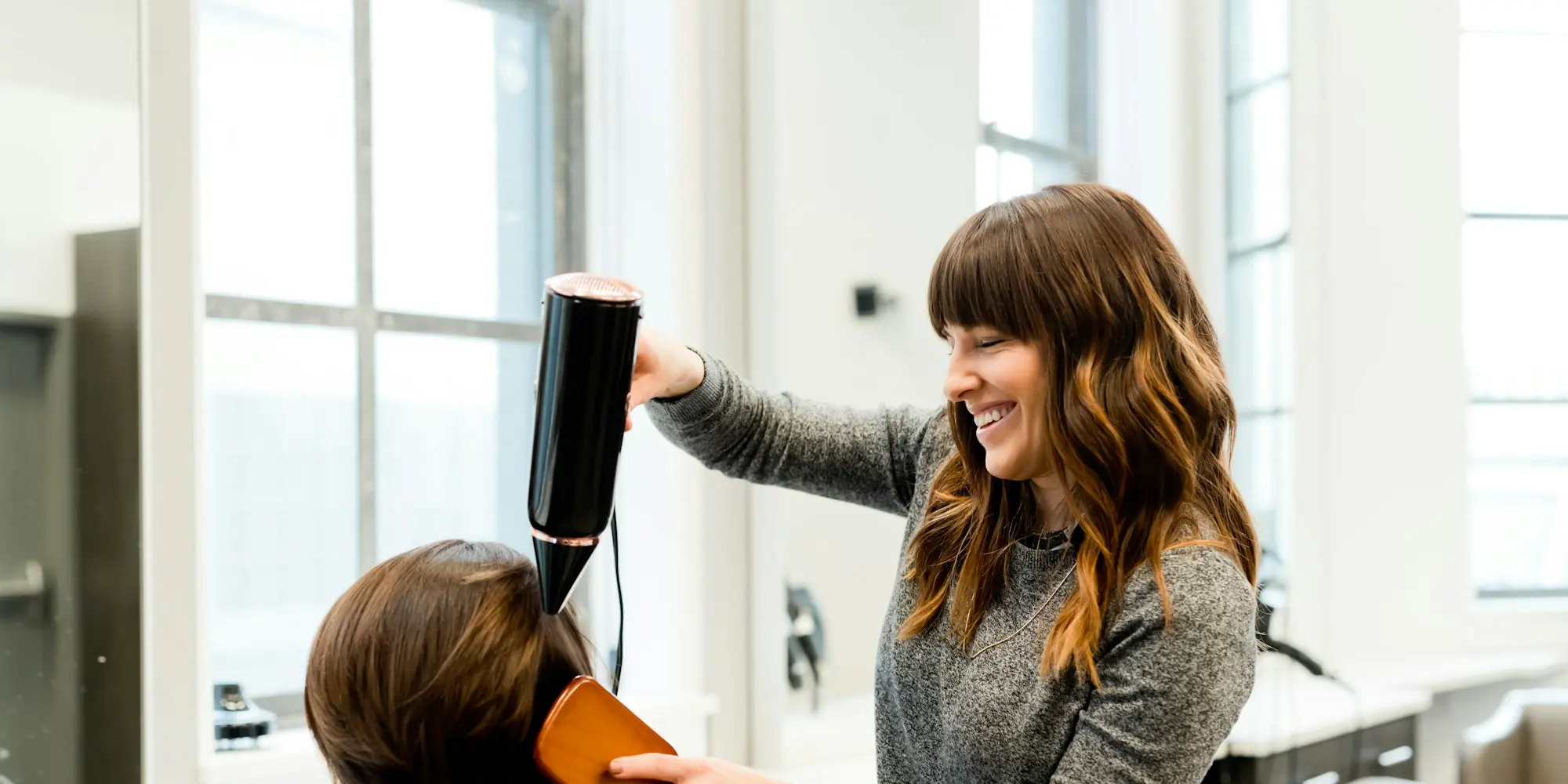 Stylist blow-drying a client's hair in a bright salon