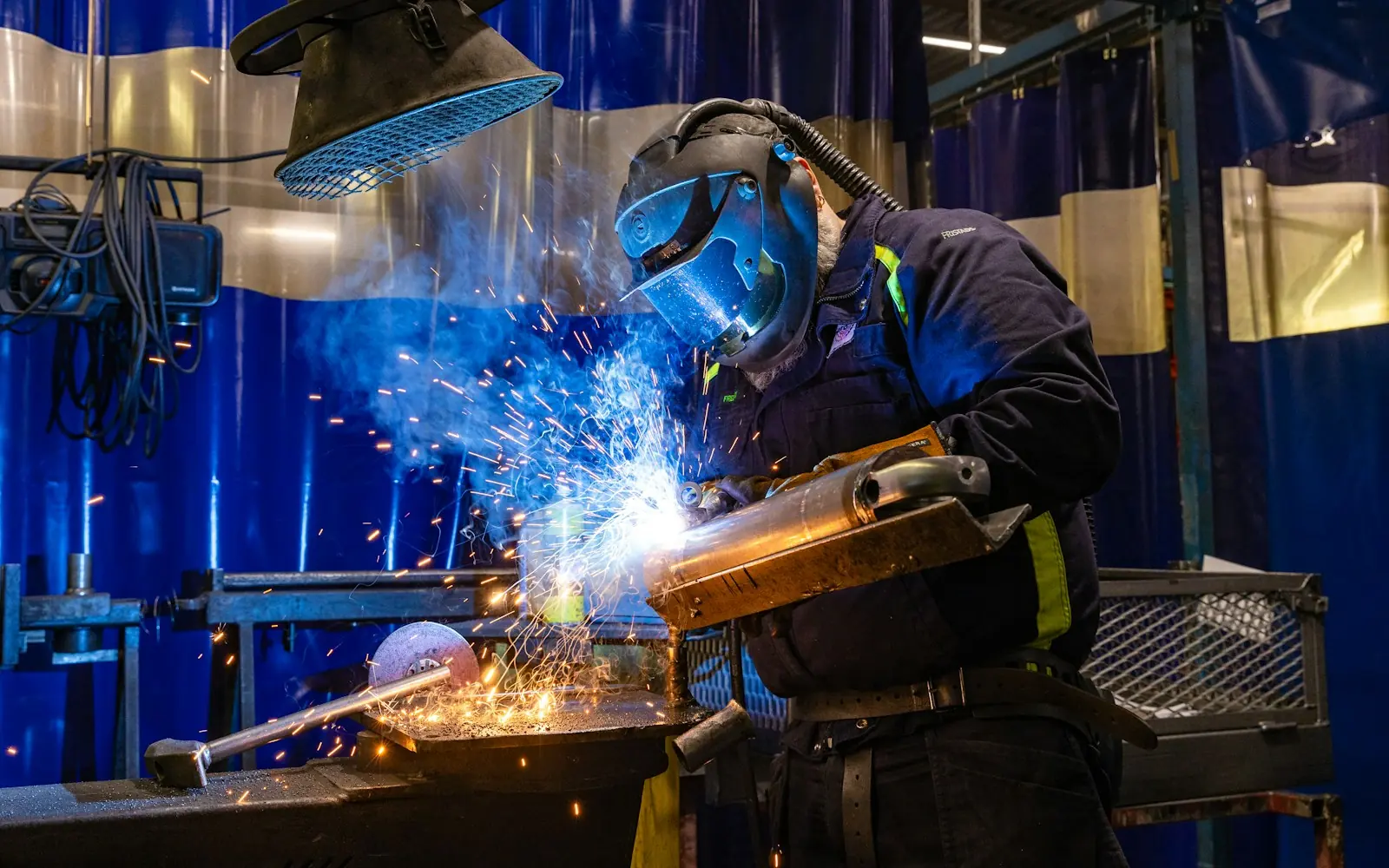 Welder in protective gear working on metal with sparks flying