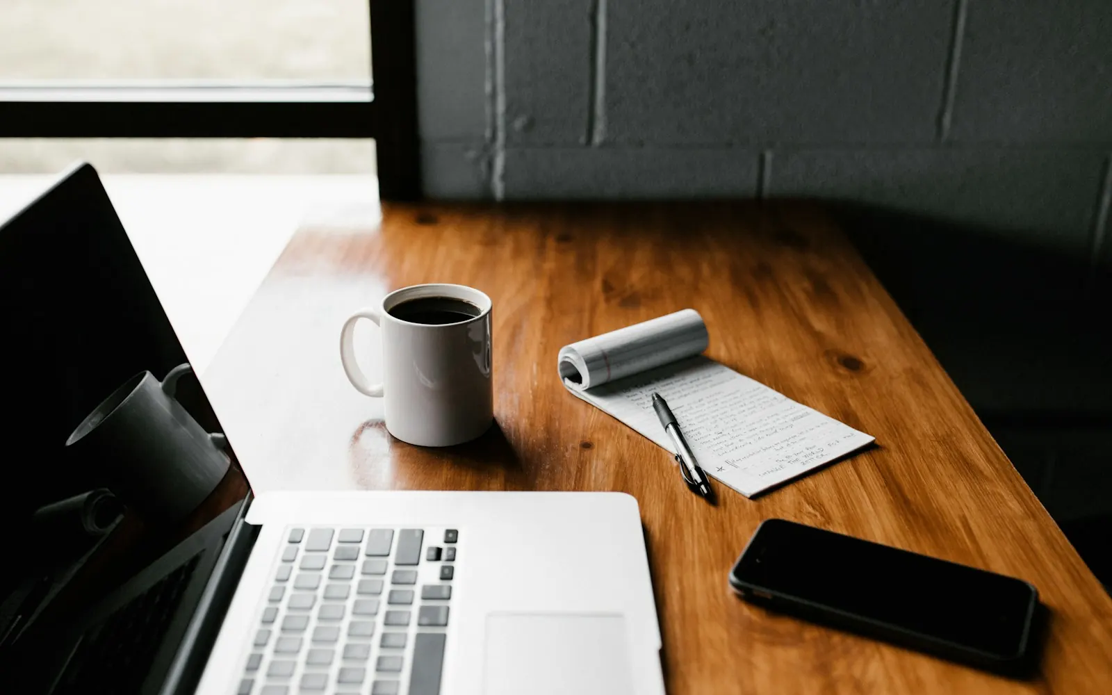Laptop, coffee mug and phone on a wooden desk