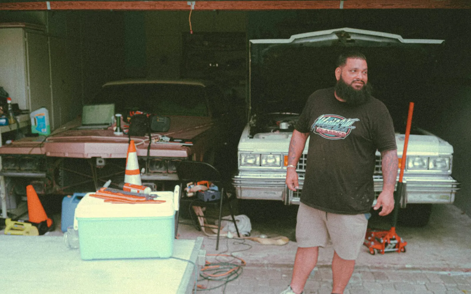 Auto repair shop owner standing in his garage in front of a classic car with its hood open
