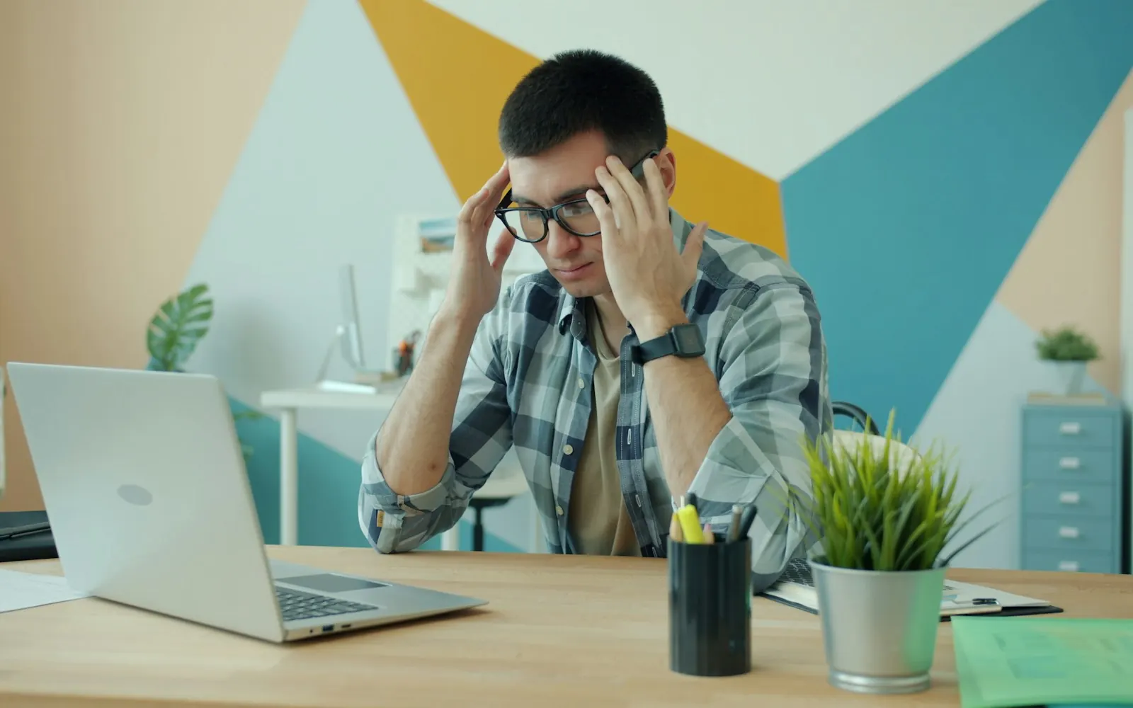 Stressed small business owner at his desk with his head in his hands in front of a laptop